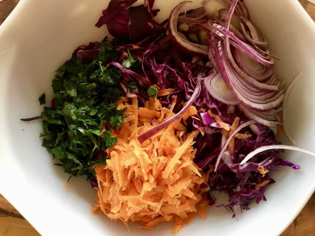shredded carrots, red cabbage, sliced onion and chopped herbs in a bowl